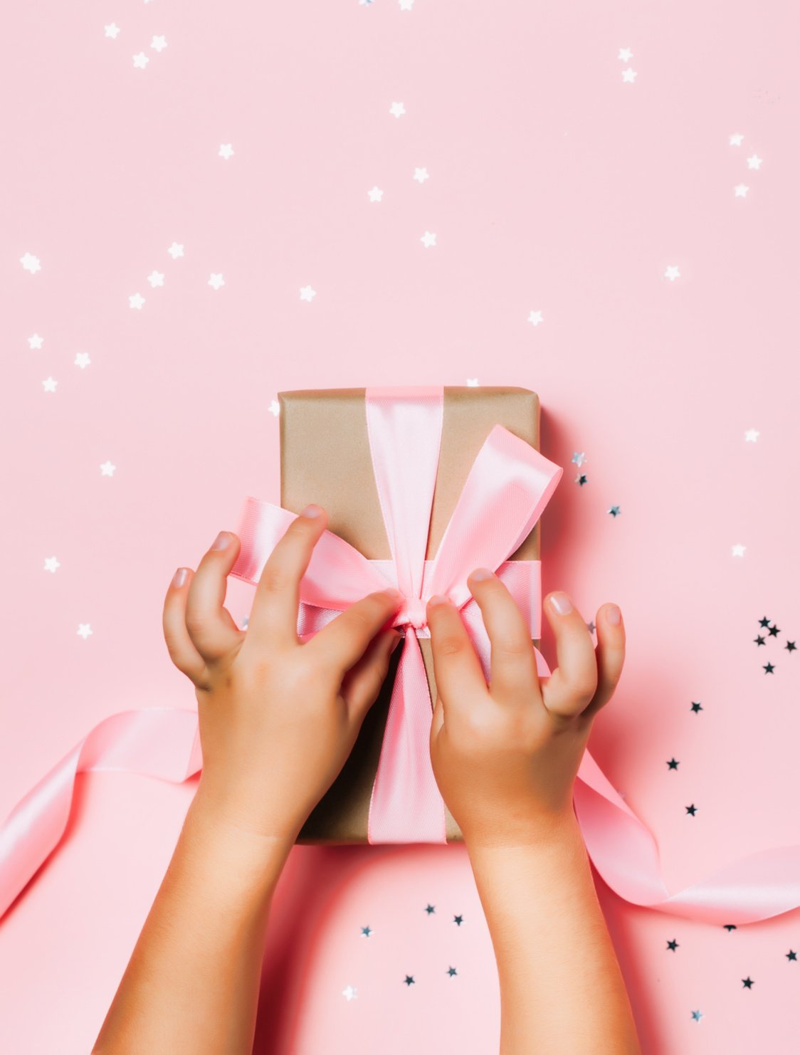 Child hands holding beautiful gift box on pink background